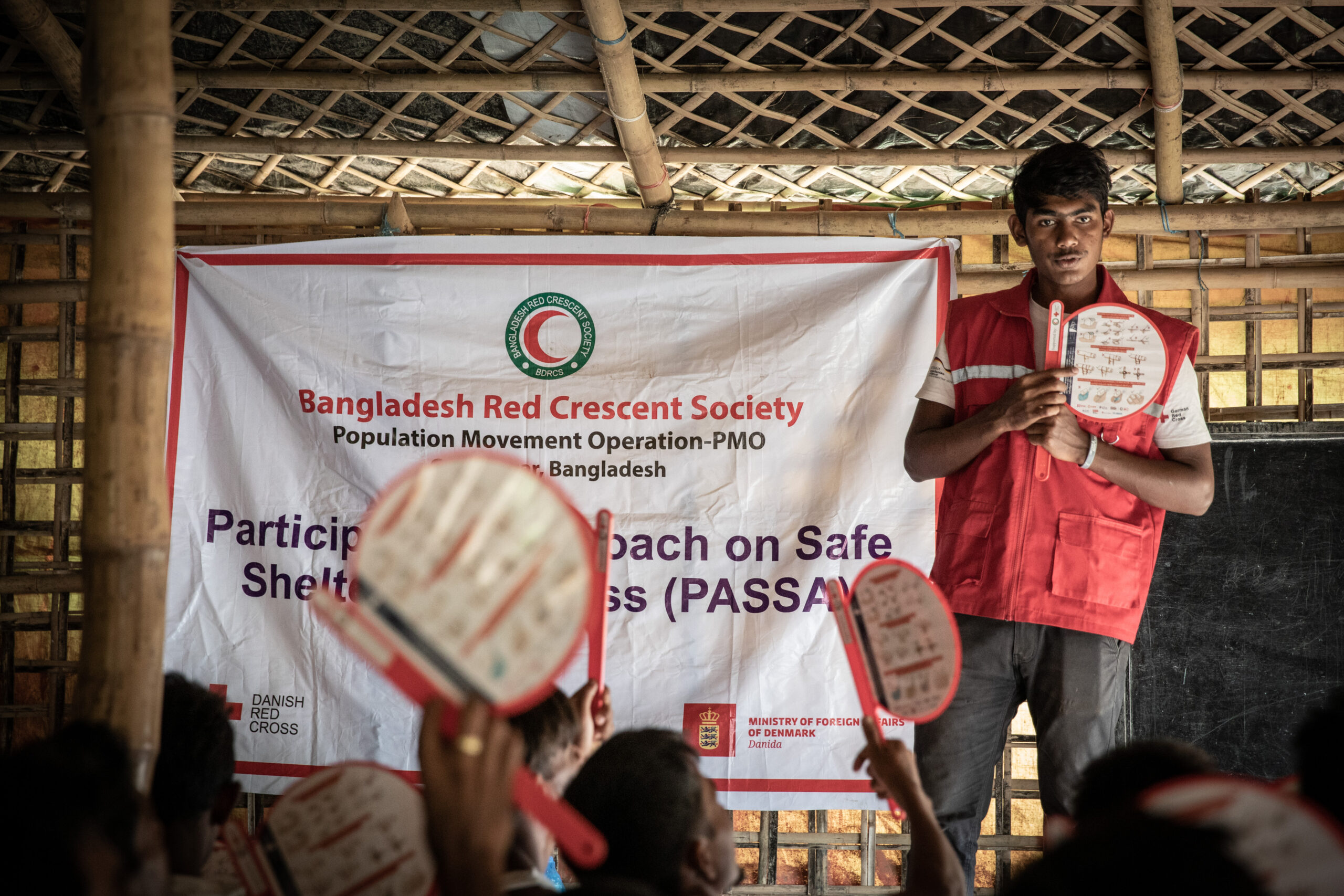 Bangladesh: Cox's Bazar, 31 July 2019
 
Abu Hanif is a Red Crescent Youth volunteer working in Camp 19. Today, he is providing training for camp residents on PASSA, participatory approach to safe shelter awareness. Bangladesh Red Crescent Society has already distributed toolkits to households to help them to secure their shelters ahead of monsoon rains or cyclones.

Hundreds of thousands of people who fled violence in Rakhine state, Myanmar, continue to live in camps in Cox's Bazar in Bangladesh. Bangladesh Red Crescent Society provides humanitarian assistance and services on a daily basis.

Photo: Stephen Ryan / IFRC